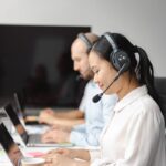 A diverse group of call center agents wearing headsets and working on laptops indoors.