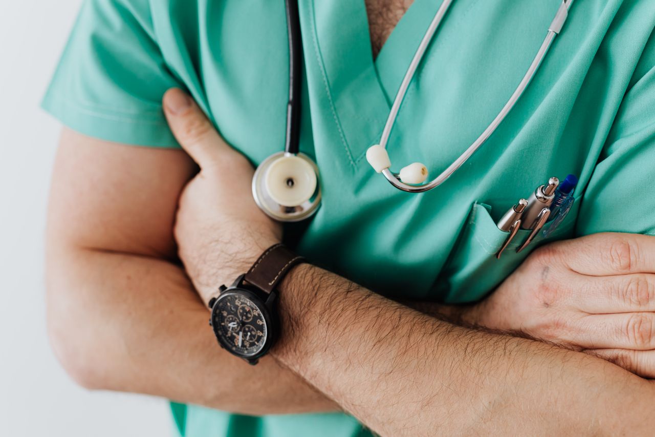 Careers Unrecognizable man wearing medical uniform with stethoscope and pens standing in hospital with crossed arms during work in day time
