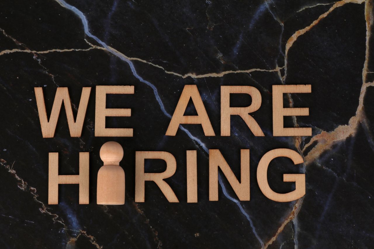 Wooden letters spell 'We Are Hiring' on dark marble surface.